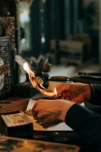 A close-up of hands burning paper amidst artistic tools, evoking creativity and mysticism.