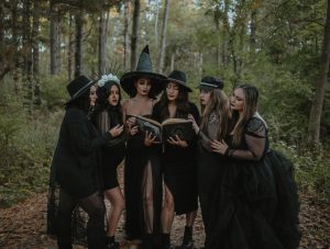A group of women in witch costumes reading a spell book amidst an enchanting forest.